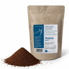 Bag of ground coffee labeled 'Venezia' with coffee grinds in front on a white backgrounds